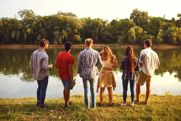 Visão traseira um grupo de jovens descansando, comunica no lago — Fotografia de Stock