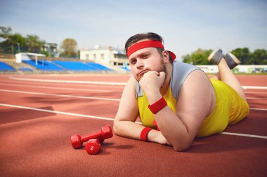 Fat funny man lying down resting on the track in the stadium clipart