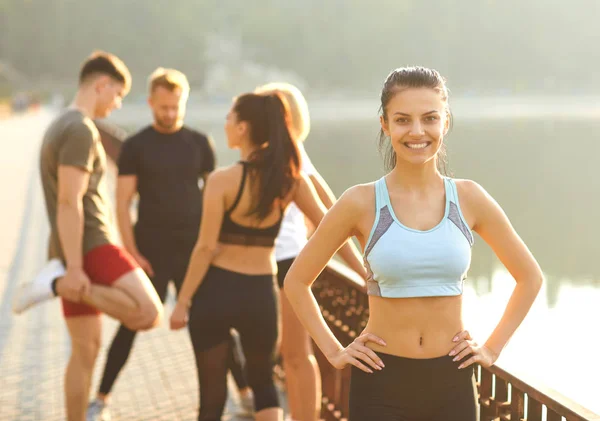 Sporty girl smiles on the background of friends athletes in the park — Stock Photo, Image