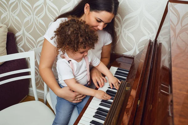 Piano lesson. Mother teacher teaches the child to play the piano