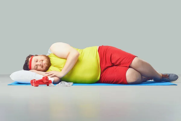 Perezoso gordo divertido hombre está durmiendo sobre un fondo gris . — Foto de Stock