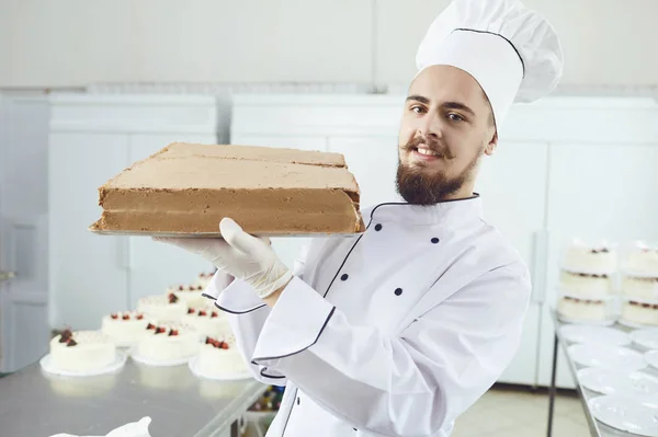 Confeiteiro homem segurando bolo sorrindo em uma pastelaria — Fotografia de Stock