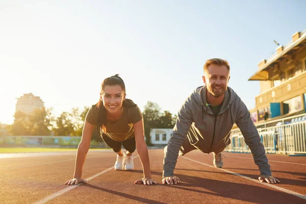 Young couple doing pushups in the stadium — Stock Photo, Image