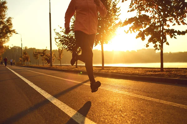 Runner runs on the road in the sun at sunset in an autumn park. — Stock Photo, Image