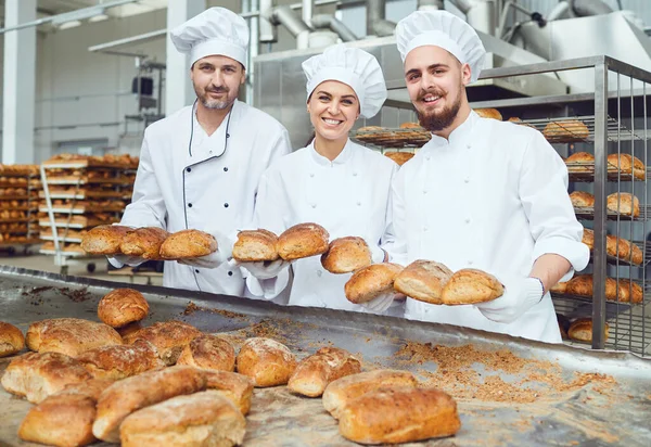 Panaderos sonriendo sosteniendo pan fresco en sus manos en una panadería —  Fotos de Stock