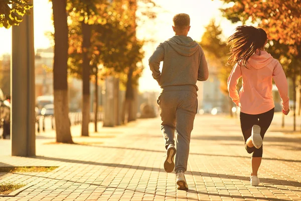 Un uomo e una donna stanno correndo lungo la strada della città la mattina . — Foto Stock