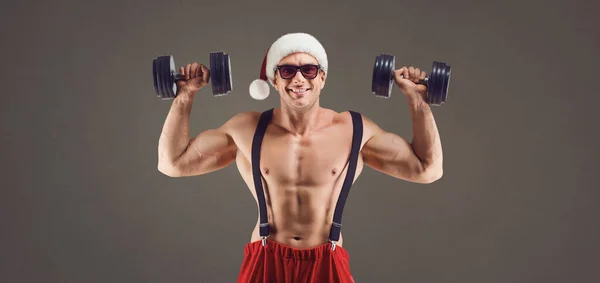 Muscular fisiculturista em Santa chapéu pressionando halteres — Fotografia de Stock