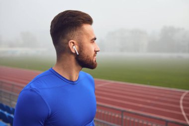 Kulaklıklı bir erkek sporcu siste stadyuma bakıyor..