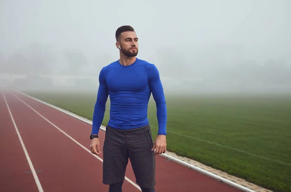 A male athlete in training stands at the stadium in the fog. — Stock Photo, Image