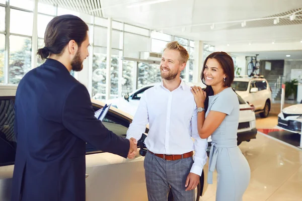 Um vendedor de carros e um comprador apertam as mãos. Um casal compra um carro — Fotografia de Stock
