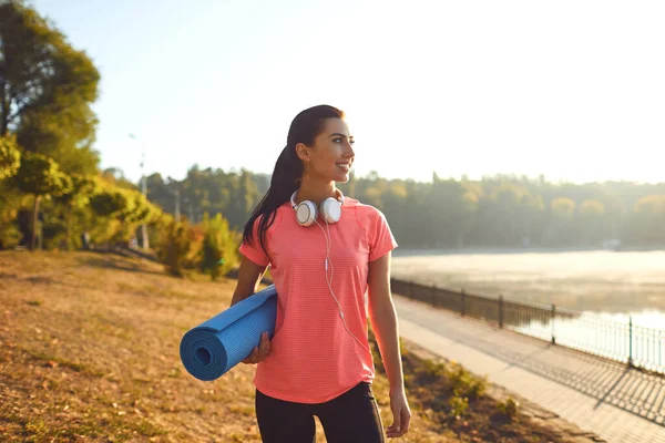 A sports girl with a yoga mat in headphones stands — Φωτογραφία Αρχείου