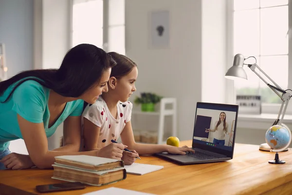 Skolan på nätet. Familj mor och flicka tittar lektion konferenslärare sitter på distans vid bordet hemma. — Stockfoto