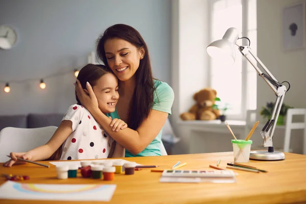 Gelukkig mam kussen knuffels dochter zitten aan de tafel in de kamer. — Stockfoto