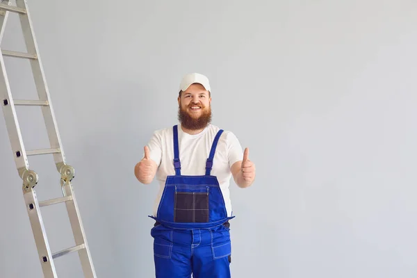 Constructor masculino optimista en uniforme cerca de escalera de metal en fondo gris — Foto de Stock