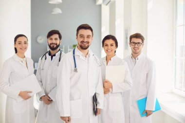 Beyaz önlüklü doktorlardan oluşan bir grup kliniğin arka planına gülümsüyor..