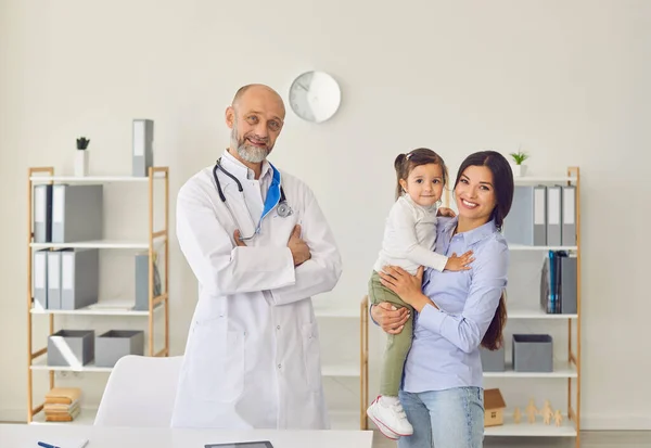 Feliz madre joven con su hija visitando al médico de familia en la clínica.Médico de familia. Pediatra senior con clientes en el hospital — Foto de Stock