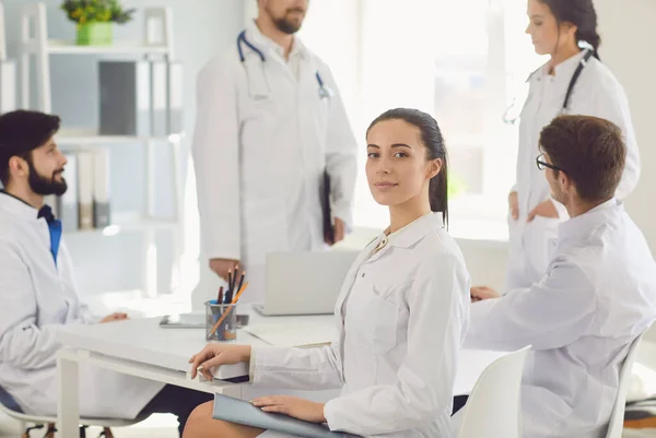 Ärztin sitzt mit Kollegen in weißen Laborkitteln an einem Tisch in einem medizinischen Krankenhaus. — Stockfoto