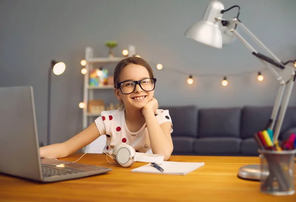 Онлайн обучение в школе. Умная счастливая девочка в очках учит лекции с помощью ноутбука в комнате . — стоковое фото