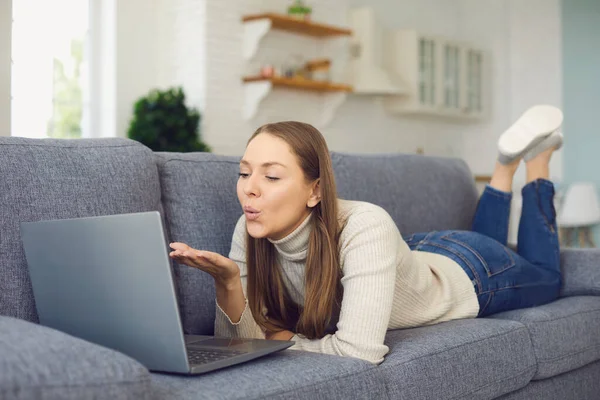 Dating online. Woman sending air kiss and using laptop in living chat room. — Stock Photo, Image