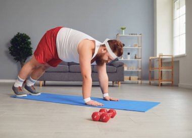 Funny red fat man doing exercises on the floor while standing at home.