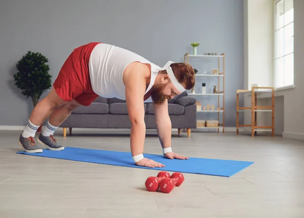 Funny red fat man doing exercises on the floor while standing at home. — Stock fotografie