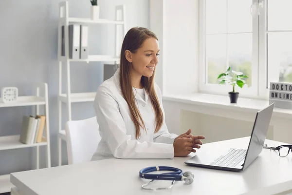 Jeune femme médecin consultant patient en ligne, en utilisant un ordinateur portable à son bureau. GP fait un appel vidéo au client malade — Photo