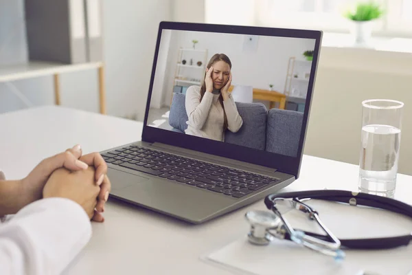 Orvos és beteg a vonalban. Az orvos egy laptop video chat konzultációt hallgat egy beteg fejfájás a kórházi irodában. — Stock Fotó