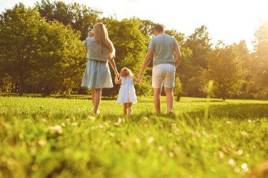 Mutlu bir aile yaz parkında çimlerin üzerinde yürüyor. Anne baba ve çocuklar doğada oynuyorlar. Çocuk Koruma Günü.