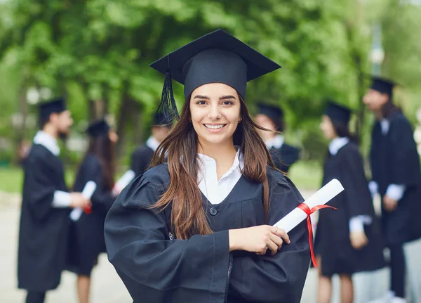 Uma jovem graduada do sexo feminino contra o pano de fundo de graduados universitários . — Fotografia de Stock