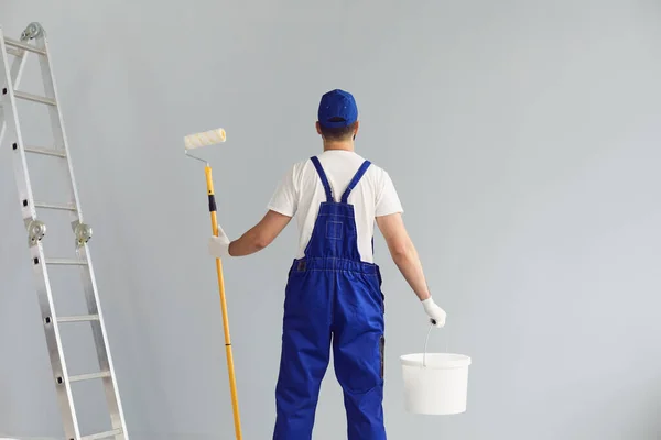 Visão traseira do trabalhador reparação home segurando escova de rolo e balde com tinta. Casa de remodelação de empreiteiro profissional — Fotografia de Stock