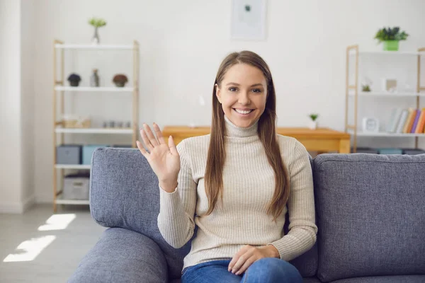 Young woman looking at the camera waving her hand online while having a laptop of call connection with a virtual man in the room. — Stock Photo, Image