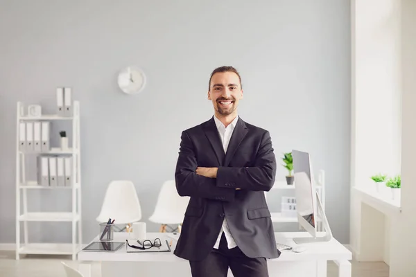 Geschäftsmann in schwarzer Jacke verschränkte lächelnd die Arme, während er im Büro stand — Stockfoto