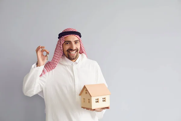 Арабский риэлтор с деревянной моделью дома в руке на сером фоне . — стоковое фото