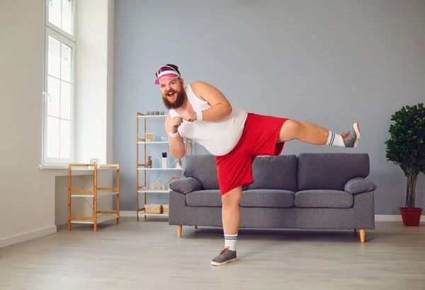 Engraçado homem gordo em shorts vermelhos e branco t-shirt sorrindo fazendo exercícios na sala — Fotografia de Stock