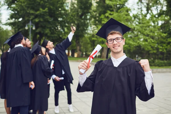 Férfi diplomás mosolyog a háttérben az egyetemi diplomások. — Stock Fotó