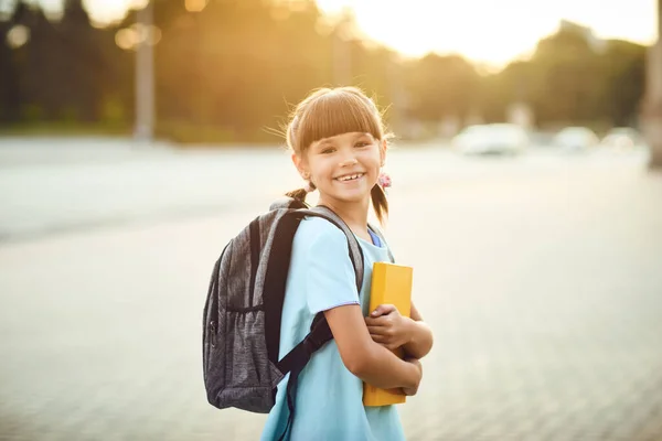 Une écolière avec un sac à dos et des livres se tient dans une rue de la ville. Retour à l'école — Photo