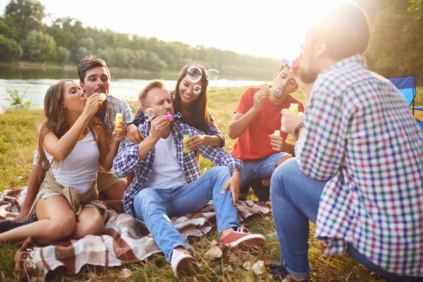 Young people make soap bubbles while sitting on the grass on in nature. — Stock Photo, Image