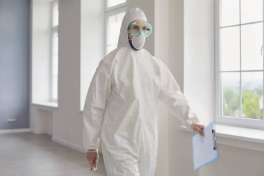 Koruyucu giysili doktor hastane koridorunda yürüyor. Tehlikeli madde giysisi içindeki doktor klinikte bulaşıcı hastalıklarla savaşıyor.