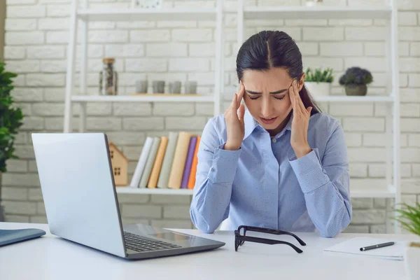 頭痛の種の女性。仕事のストレスのために頭痛を持っているラップトップコンピュータと自宅のオフィスで女性の専門家. — ストック写真