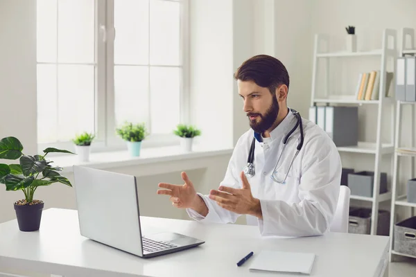 Mężczyzna lekarz świadczący konsultacje medyczne za pośrednictwem wideokonferencji przy użyciu laptopa w biurze. — Zdjęcie stockowe