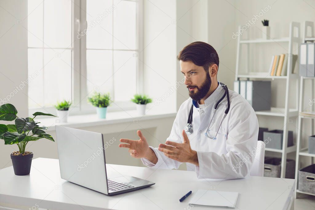 Male doctor providing medical consultation via video conference using laptop computer in office.