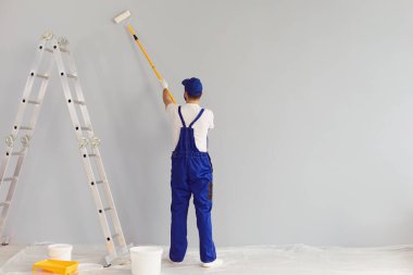İşçi ressam bir duvar boyuyor. Arka plan. Profesyonel inşaatçı tamirat yapar..