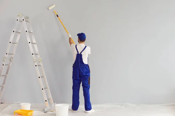 Ζωγράφος εργάτης ζωγραφίζει έναν τοίχο.Πίσω όψη. Επαγγελματική οικοδόμος κάνει επισκευές. — Φωτογραφία Αρχείου