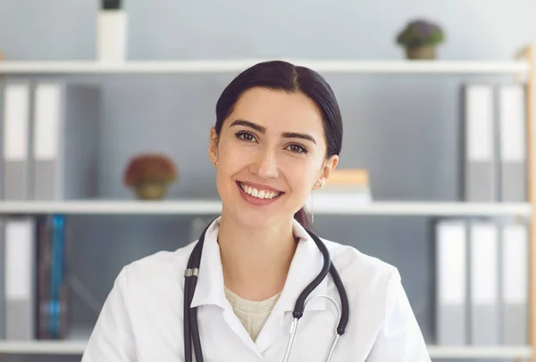 Portret pięknej młodej lekarki patrzącej w aparat fotograficzny w gabinecie lekarskim, po konsultacji online z pacjentem — Zdjęcie stockowe