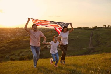 Neşeli aile, bir yaz parkında çimlerin üzerinde koşarken eğleniyor. ABD 4 Temmuz Kutlaması.