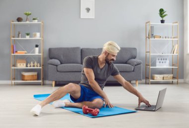 Çevrimiçi eğitim kursunda egzersiz yapan genç adamın evinde dizüstü bilgisayarı var. Uzaktan spor eğitimi..