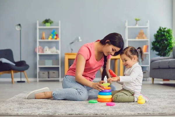 Jonge moeder en haar dochter betrokken bij een interessant spel op de vloer thuis. Ouder en kind spelen met piramide binnen — Stockfoto