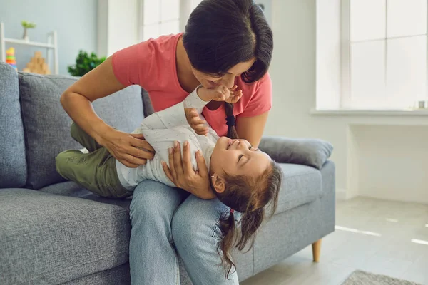 Glückliche Mutter und Tochter beim Umarmen und Spielen auf dem Wohnzimmersofa. Epidemische Isolation der Familie zu Hause. — Stockfoto