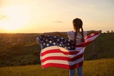 Bağımsızlık Günü ABD. Gün batımında Amerika 'nın bayrağını taşıyan bir kızın arka görüntüsü..