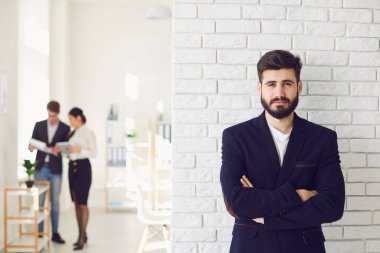 Beyaz bir ofis geçmişine bakarak gülümseyen ceketli mutlu sakallı bir iş adamı..